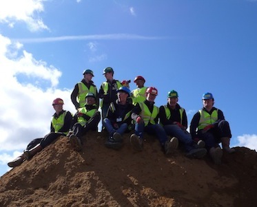 Group of young people wearing hard hats sitting on an earth mound. Photo taken at Build Camp