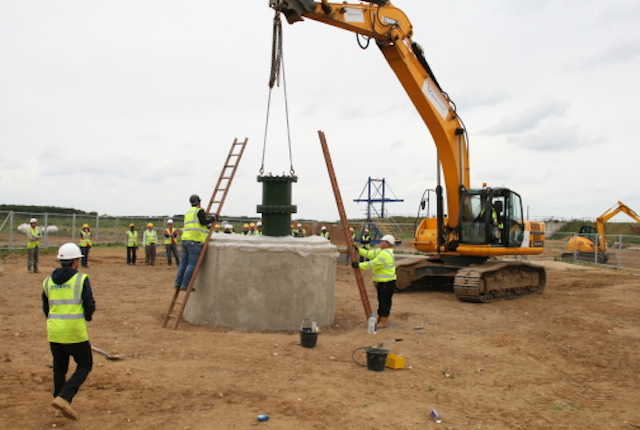 An excavator is used to lift a steel pressure vessel into a cylindrical concrete chamber
