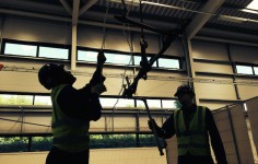 Two students use a block and tackle to lift a pipe over their heads.