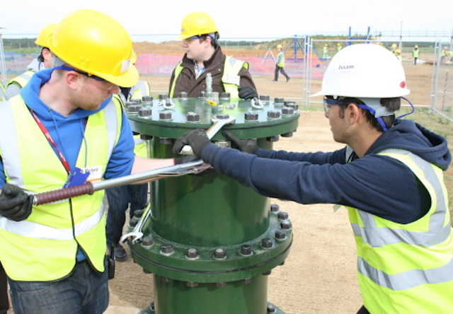 Three students in hard hats use a large spanner to tighten bolts on a steel pressure vessel
