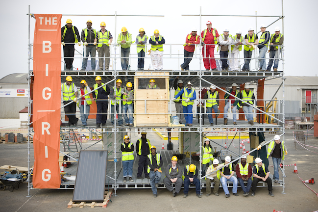 Image showing a three-storey scaffolding frame, called the Big Rig, on which forty people are smiling for a photograph.